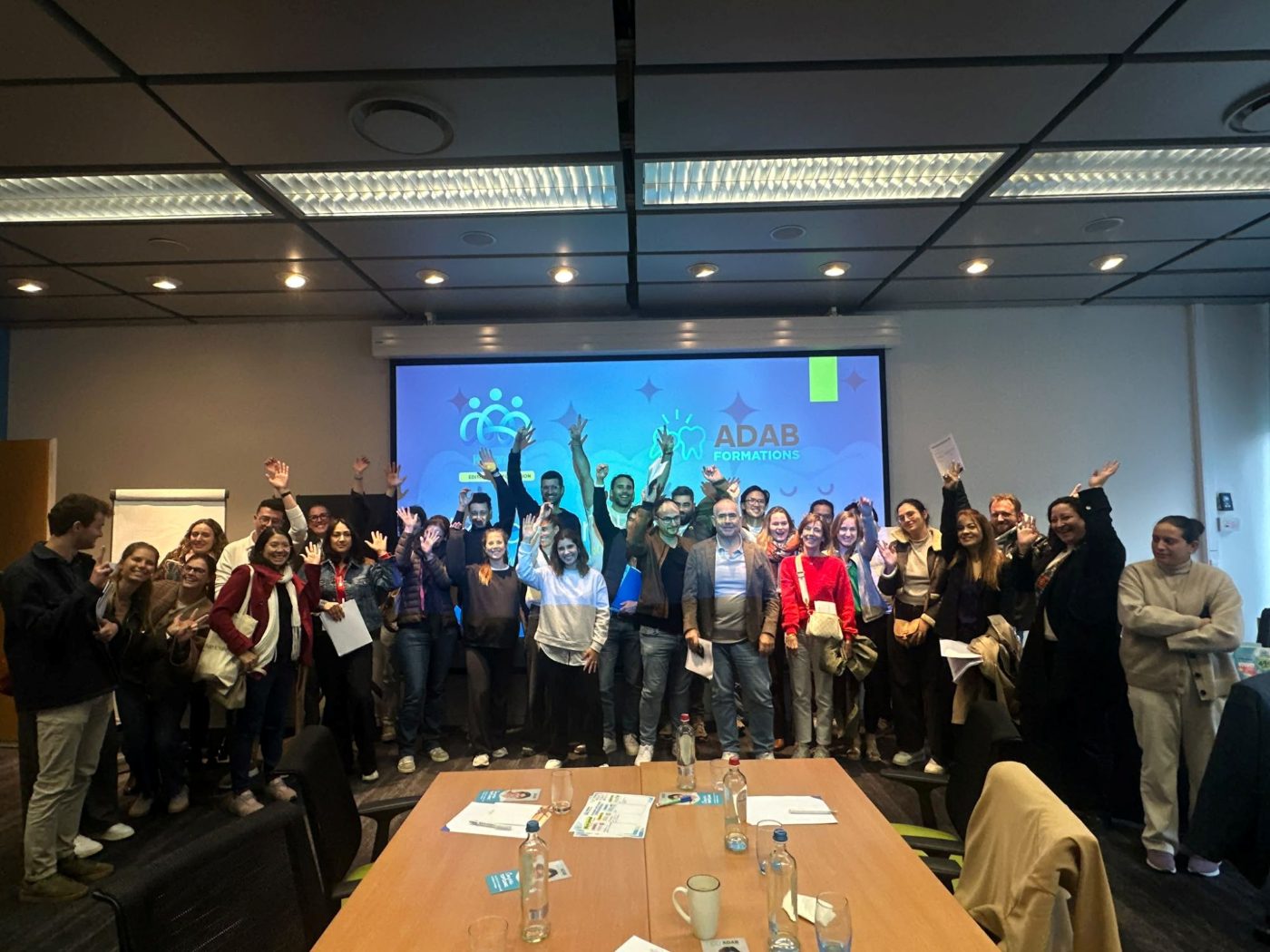 Un grand groupe de participants, bras levés, à la fin d'une formation